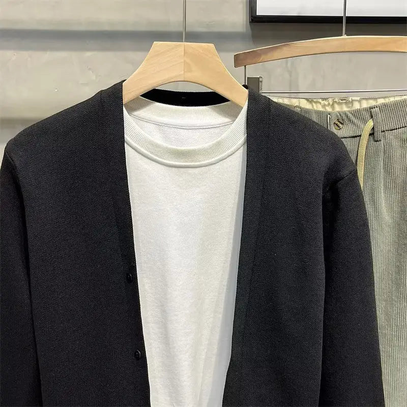 Herren-Strickcardigan in Dunkelgrau mit schwarzer Knopfleiste, getragen über einem weißen Rundhalsausschnitt.
