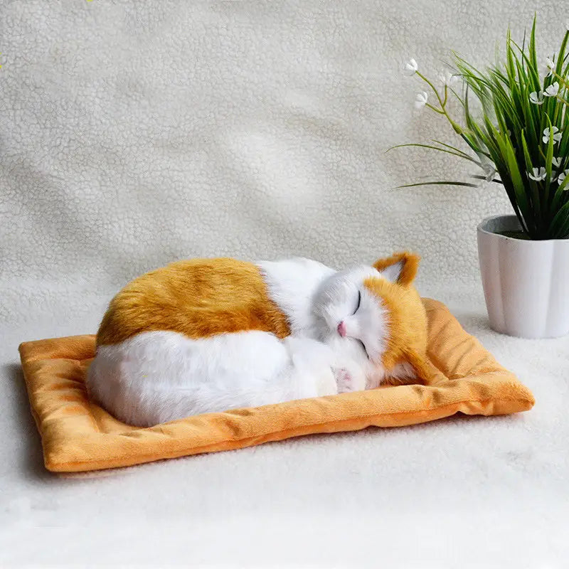 A realistic breathing plush cat figurine featuring an orange and white calico design curled up in a cozy sleeping pose on an orange cushion pet bed.