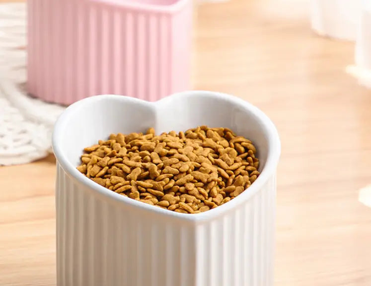 White heart-shaped ceramic pet food bowl with vertical ridges filled with brown kibble from the tilted ceramic cat bowl set 4 pack.