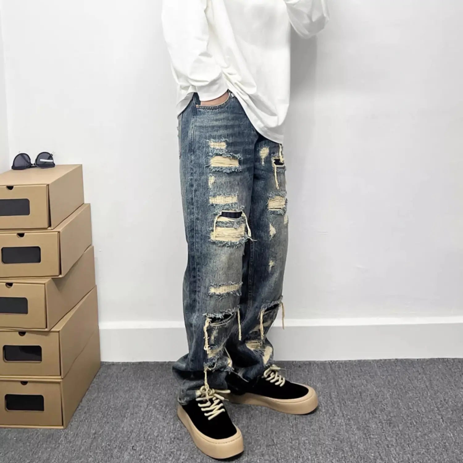 Men’s light blue distressed ripped patch denim jeans featuring multiple frayed and ripped sections on blue denim fabric.