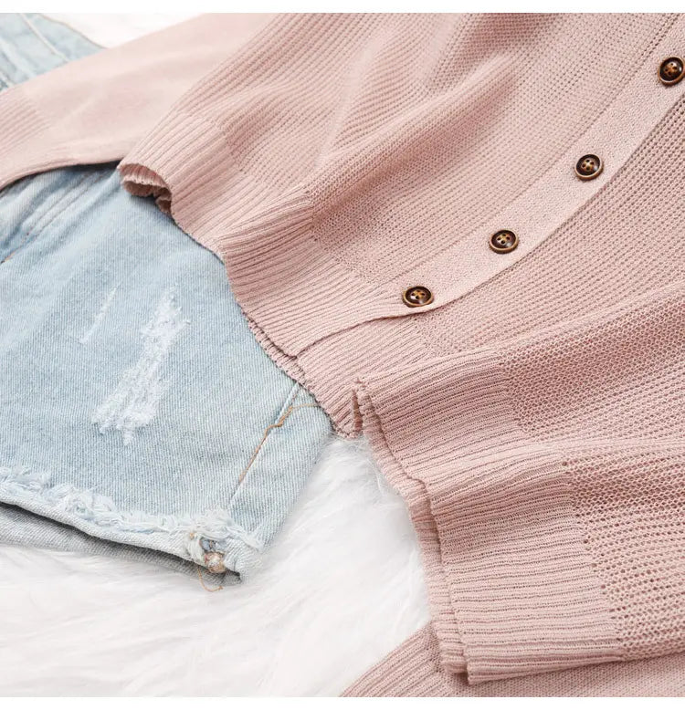 Ein weichrosa gestricktes Hoodie-Cardigan mit gerippter Strickstruktur und braunem Knopfverschluss.