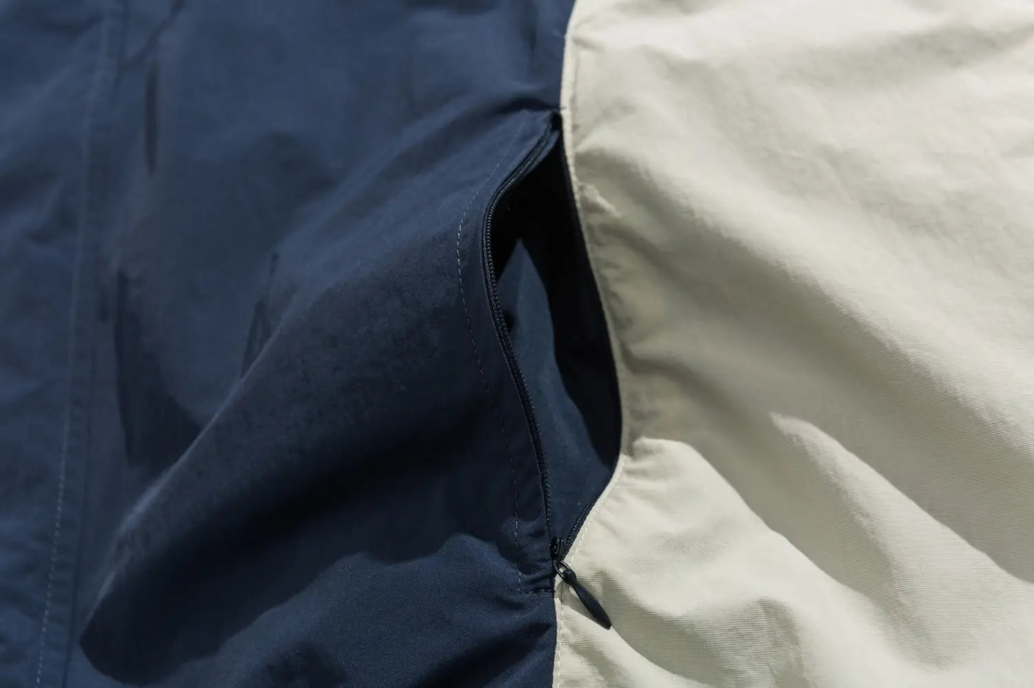 Veste coupe-vent ample à blocs de couleurs brodés bleu marine et crème, dotée d’une poche zippée pour une utilisation extérieure légère.