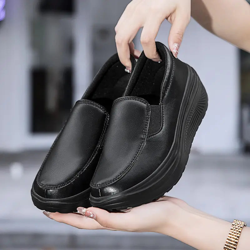 Chaussures slip-on à talon compensé en forme de coin en cuir noir, avec une semelle épaisse texturée, présentées depuis le côté arrière