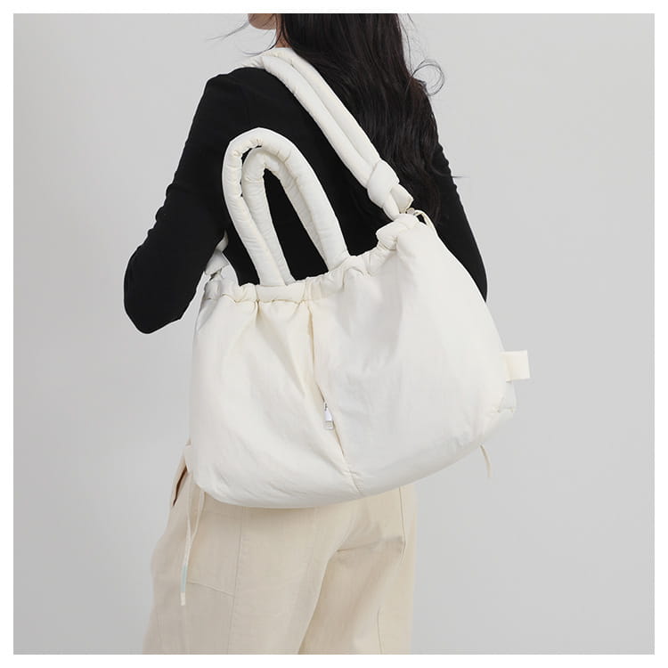 White quilted puffer tote bag made of lightweight nylon with thick padded handles and a drawstring closure.