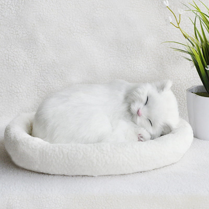 A plush white cat figurine with realistic breathing feature nestled in a matching fluffy white pet bed.