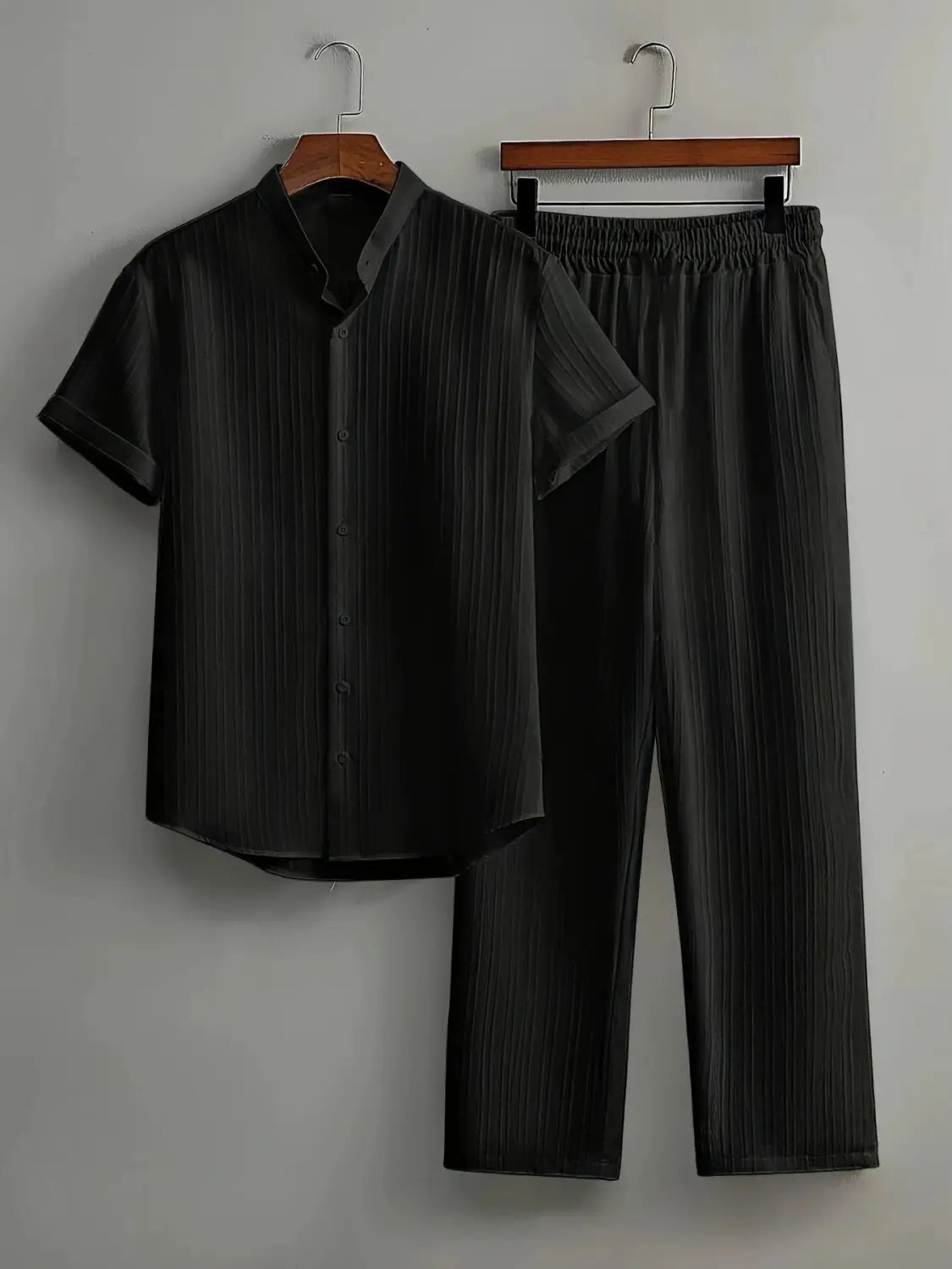 black mens short-sleeved button-up shirt and matching pleated pants set made of smooth slightly glossy fabric with subtle vertical ribbing