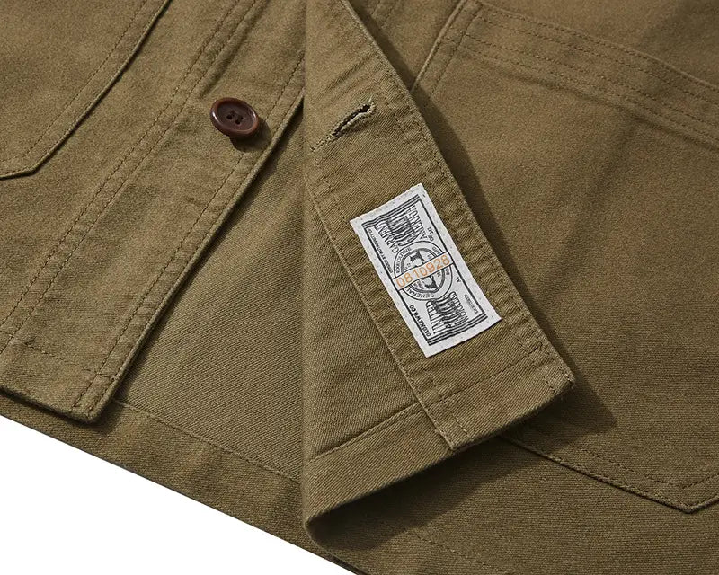 Mens french workwear jacket in olive green canvas with a brown button and white label on the collar featuring cotton utility pockets.