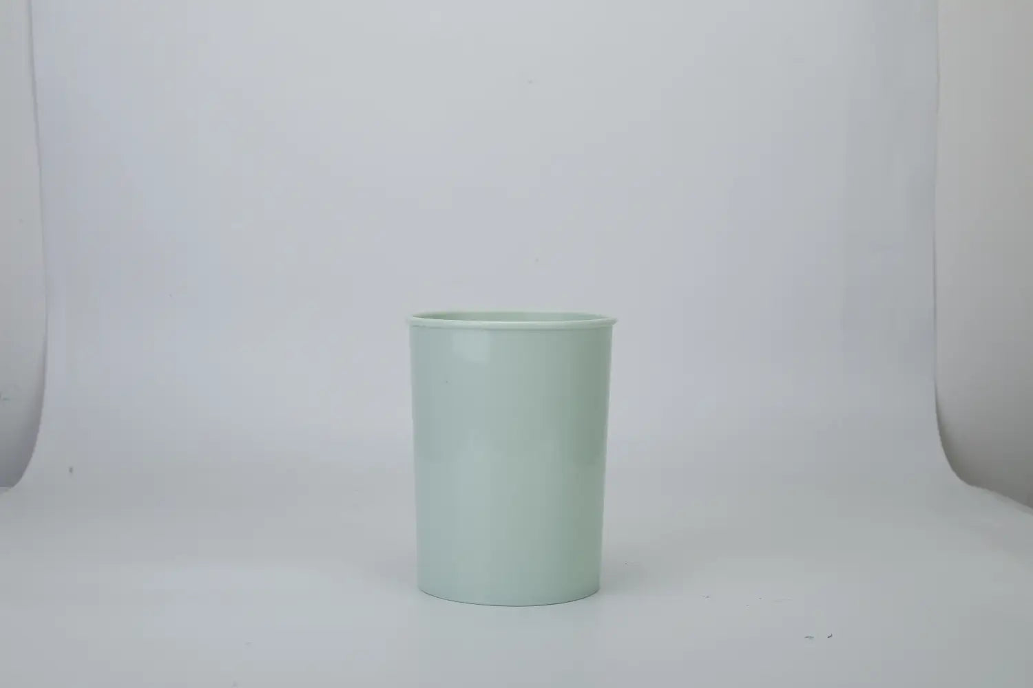 A sleek light green ceramic toothbrush holder with a smooth glossy finish and simple cylindrical design displayed alongside an 11 piece silicone cooking utensil set with wood handles.
