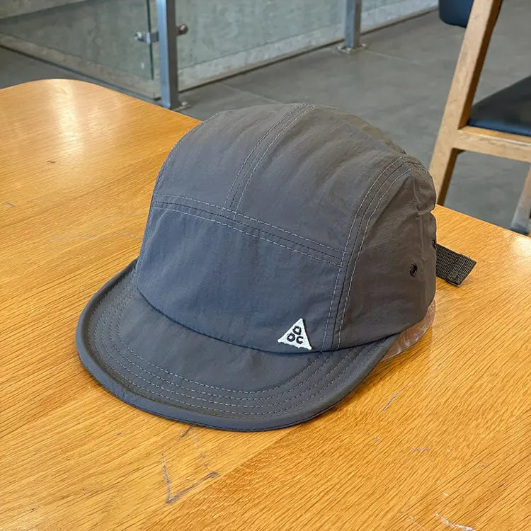 Dark gray quick drying five panel cap with short brim and white triangular logo on the front.