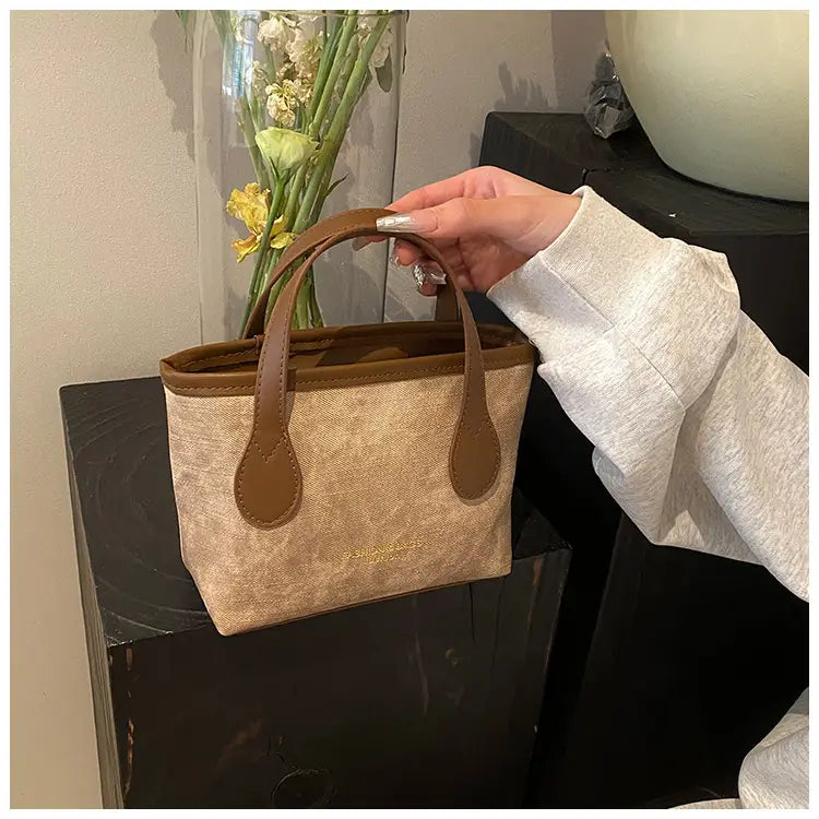 Beige canvas mini tote with brown leather handles and trim featured as a retro bucket bag textured canvas shoulder handbag.