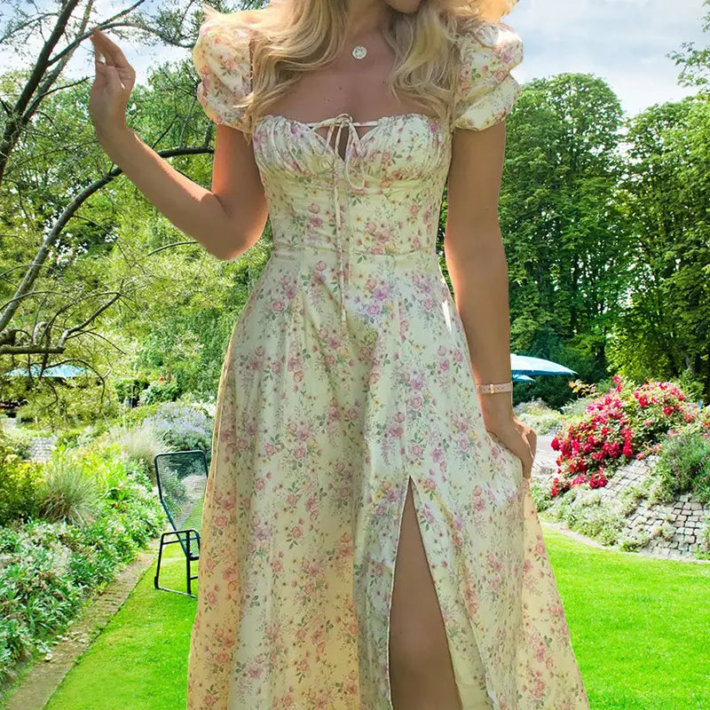 A flowing off-white floral midi dress with puffed short sleeves and a corset-style bodice featuring a square neck and a slit.