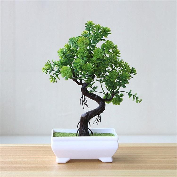 Ein miniaturisiertes künstliches Bonsai-Bäumchen mit üppigem grünem Laub und dunklem, gedrehtem Stamm sitzt stilvoll in einem eleganten weißen Keramiktopf.