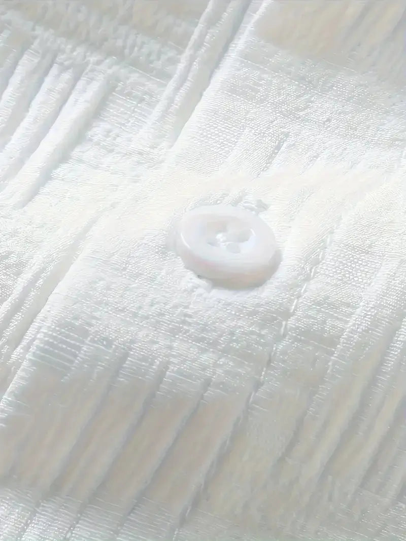 Un bouton blanc délicat, avec une légère brillance, est mis en avant sur un ensemble chemise et short pour homme à manches courtes texturées, réalisé dans un tissu doucement plissé
