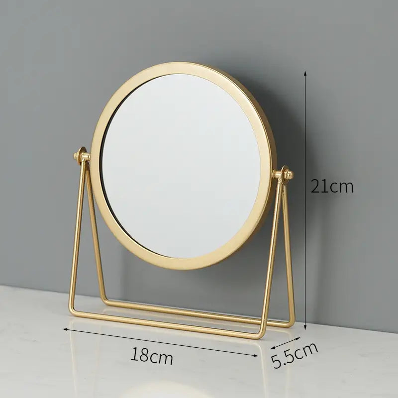 Gold-finished round vanity mirror with a minimalist triangular metal stand designed for makeup and desk use.