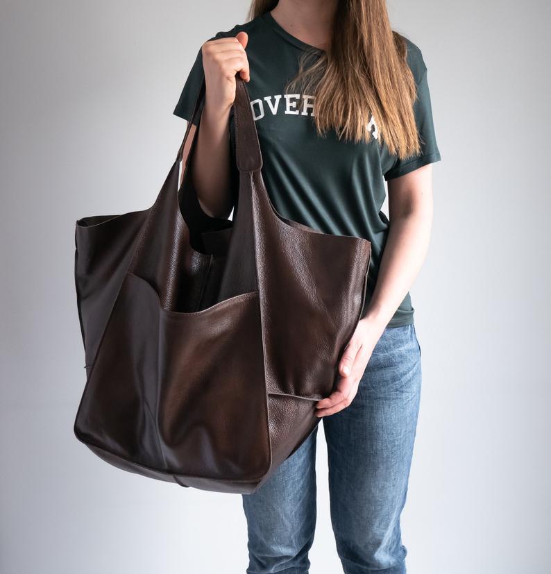 Brown leather tote bag with soft textured surface and wide handles designed for large capacity and slouchy shoulder use.