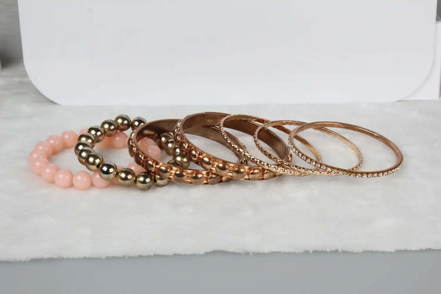 A collection of rose gold and metallic retro gold and pink rhinestone bangle bracelets featuring beaded textured and pave designs alongside a soft pink bead bracelet.