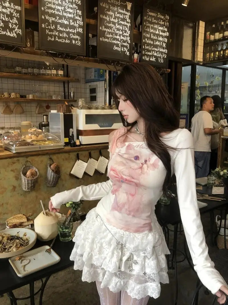 White long-sleeved top with pink cat print paired with a lace ruffle skirt featuring delicate detailing.