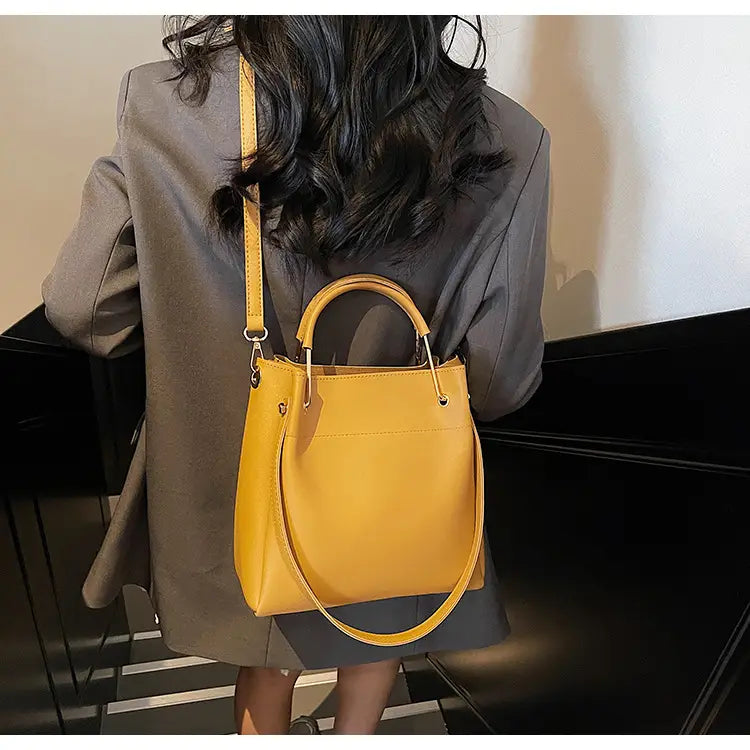 A vibrant yellow minimalist leather bucket bag with a structured rounded body, matching top handle, and detachable strap.