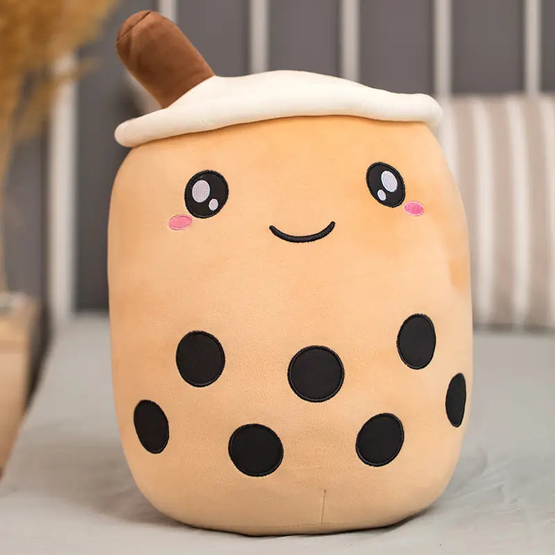 cute beige plush toy shaped like a boba milk tea cup with black tapioca pearls embroidered eyes and blush cheeks made of soft material designed as a hugging pillow