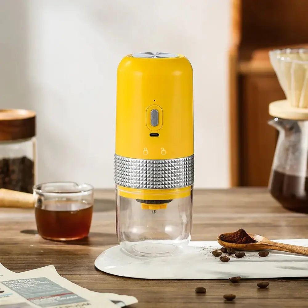 Bright yellow compact automatic electric coffee grinder with textured silver metallic band and clear glass base