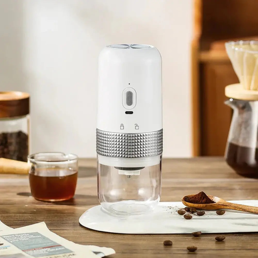 Compact automatic electric coffee grinder in white and silver with textured metallic band and clear glass base for grounds