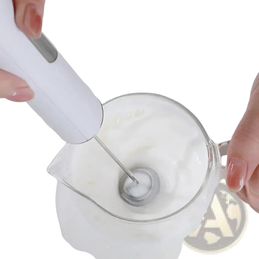 White handheld electric milk frother with silver metal whisk head whipping cream in a clear glass pitcher