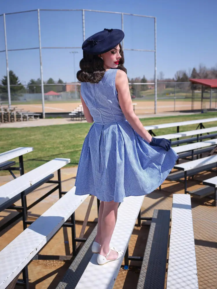 A woman wears an Elizabeth blue gingham vintage cotton dress with a fitted bodice flared skirt and pockets
