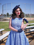 A woman wearing an Elizabeth blue gingham vintage cotton dress with button-front neckline and matching navy gloves