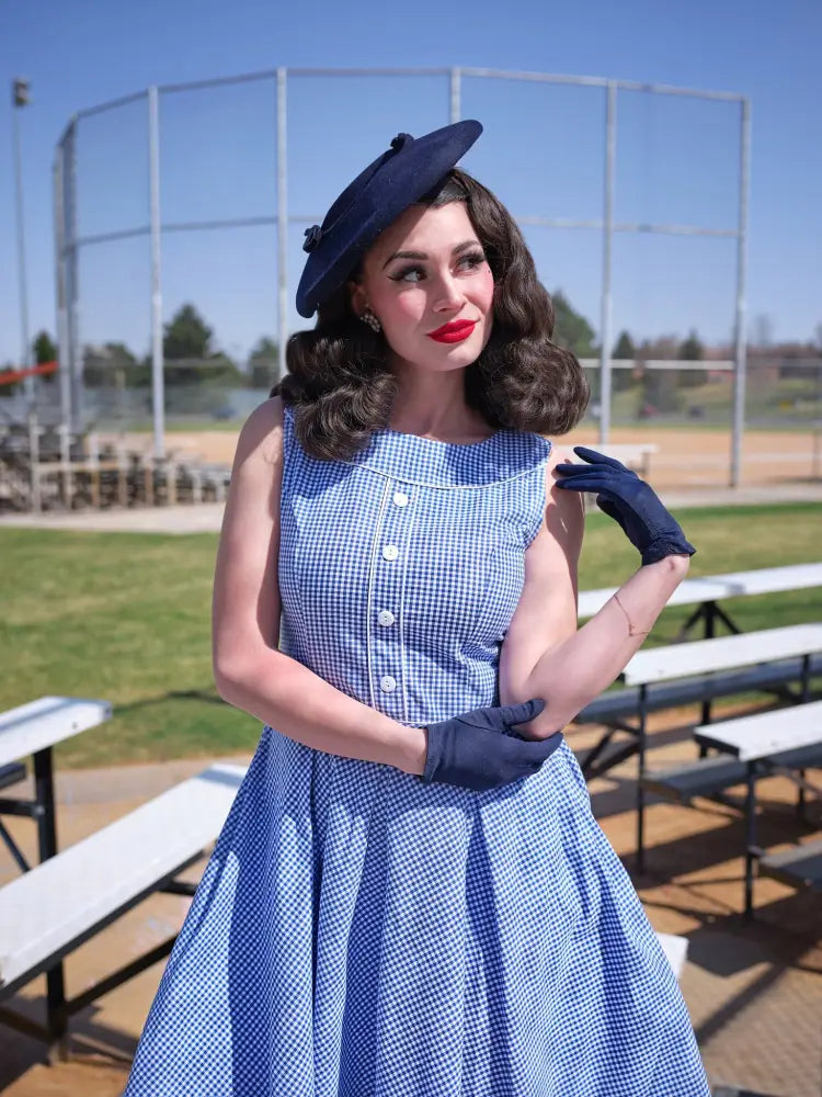 A woman wearing an Elizabeth blue gingham vintage cotton dress with button-front neckline and matching navy gloves
