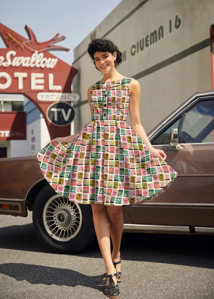 A vibrant sleeveless a-line cotton dress featuring a colorful vintage postage stamp print in pink green yellow and blue