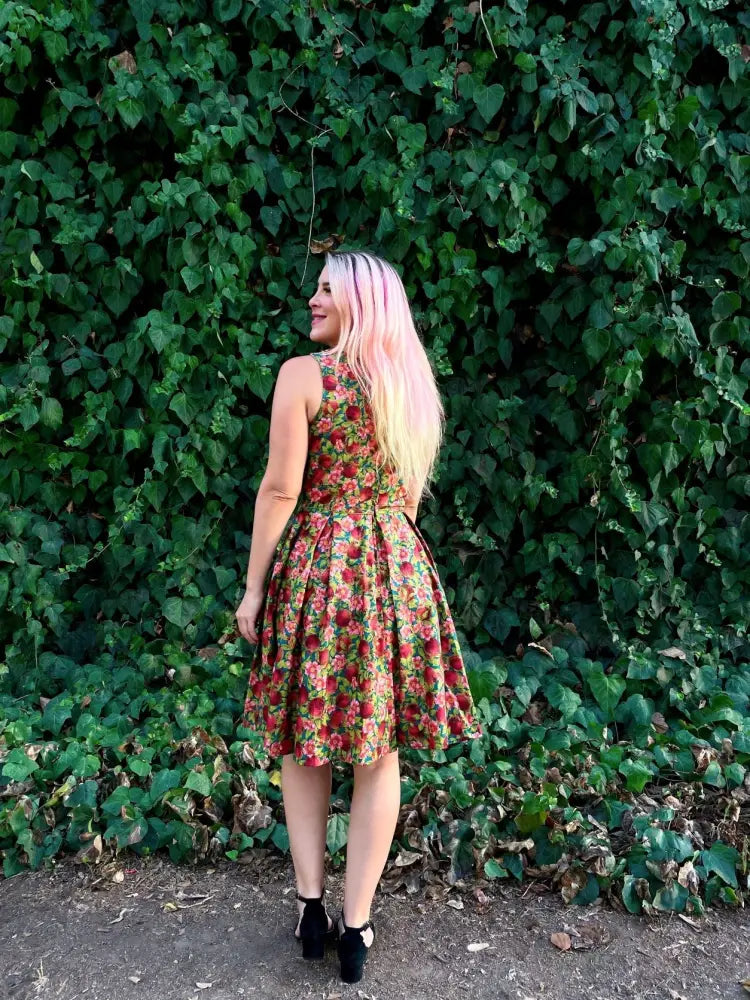 A woman wearing an elizabeth pomegranate floral cotton a line vintage dress with vibrant red and green floral pattern