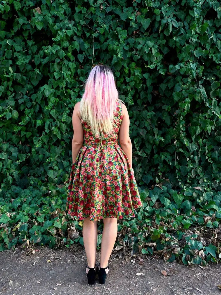 A woman wearing an Elizabeth Pomegranate floral cotton a-line vintage dress with red and green roses on beige