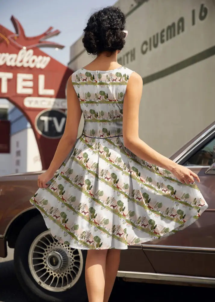 Elizabeth dress in woodland sunset cotton print featuring a white sleeveless fitted bodice and flared skirt with green trees and brown deer pattern