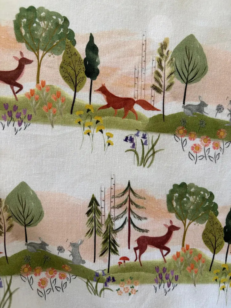 Elizabeth dress in woodland sunset cotton print featuring white fabric with soft green brown and pastel pink woodland scene