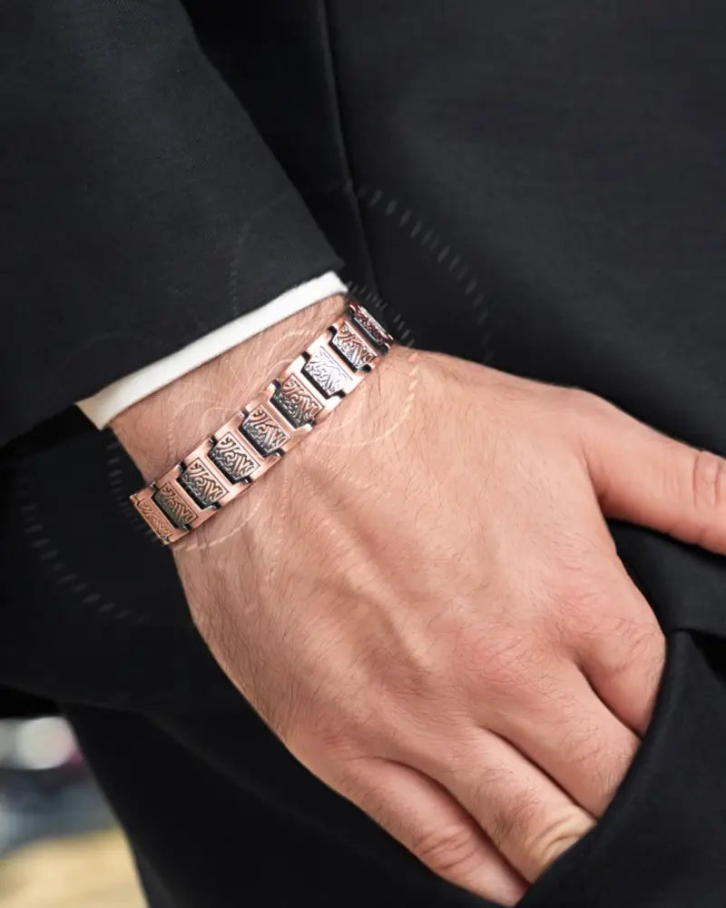 A sleek rose gold magnetic copper bracelet with an intricate geometric pattern worn on a mans wrist by Ellipsemax