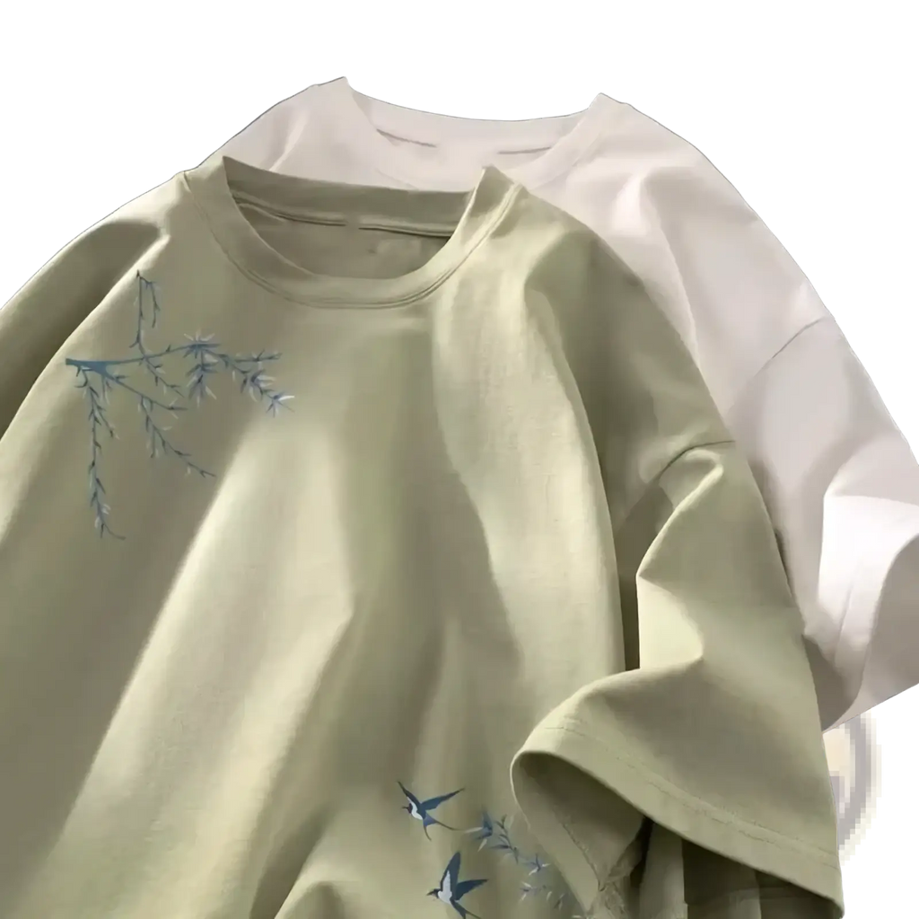 A soft sage green cotton oversized t-shirt with delicate blue embroidered branches and birds