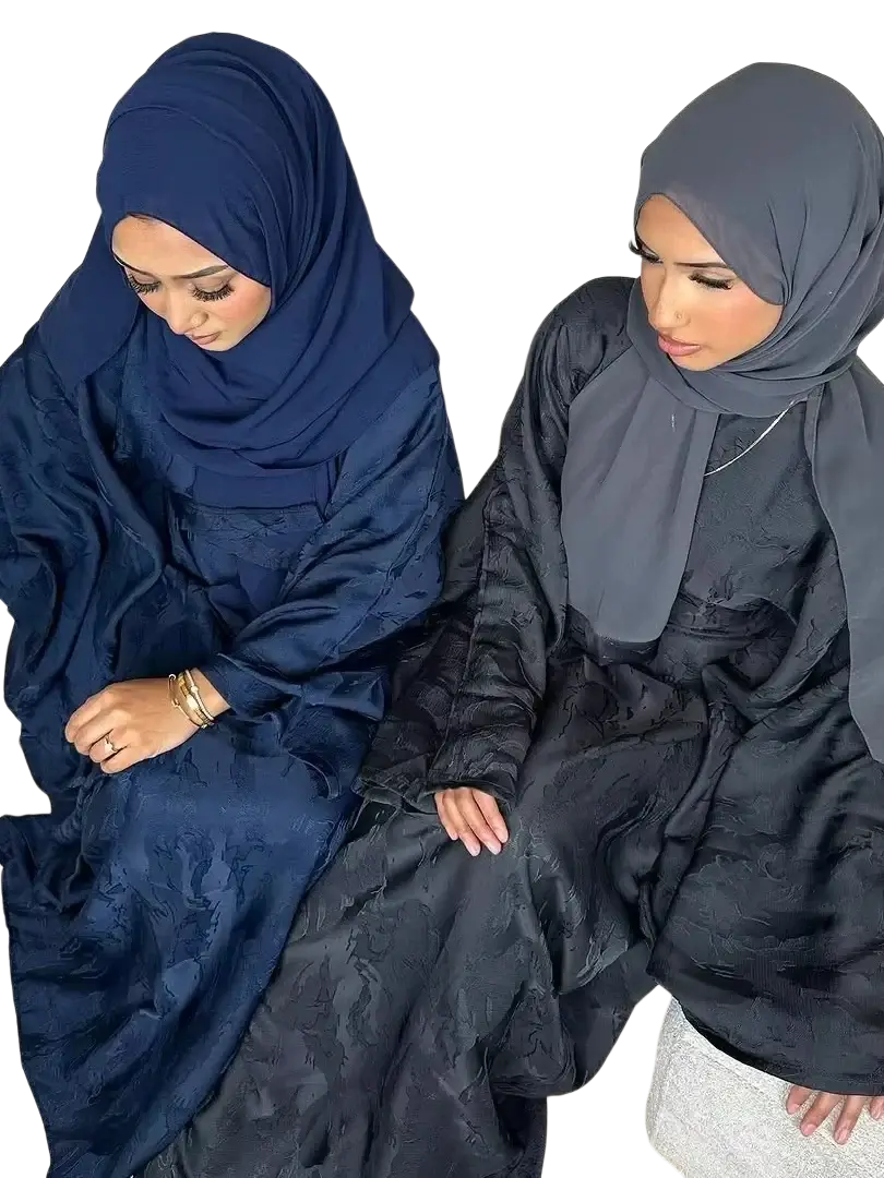 Two women seated on a couch wearing elegant embroidered floral abaya kaftan maxi dresses with hijabs