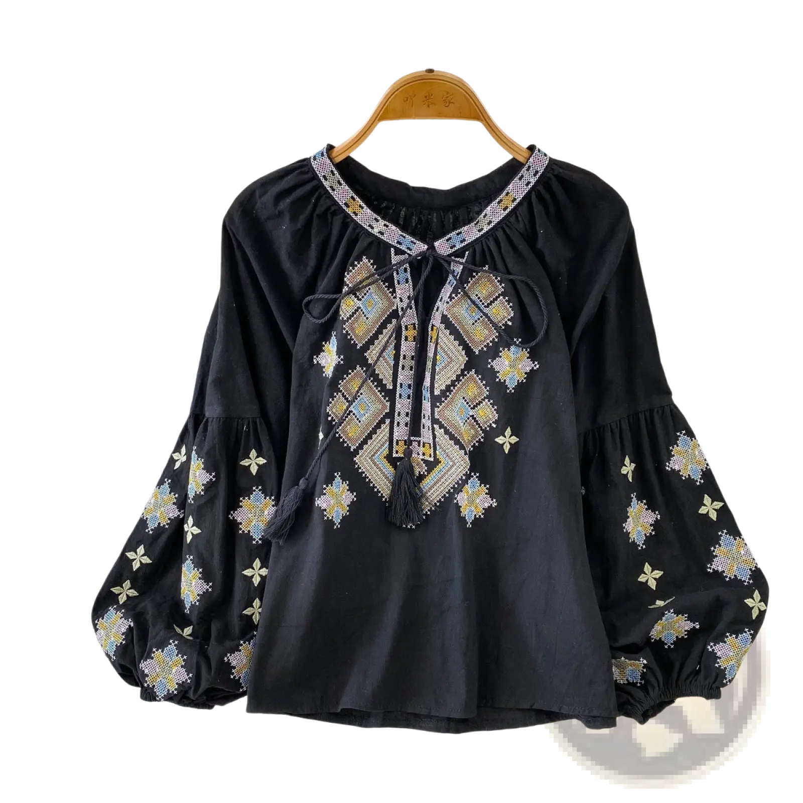 Black embroidered lantern sleeve blouse with intricate gold blue and white geometric patterns and tie front tassels