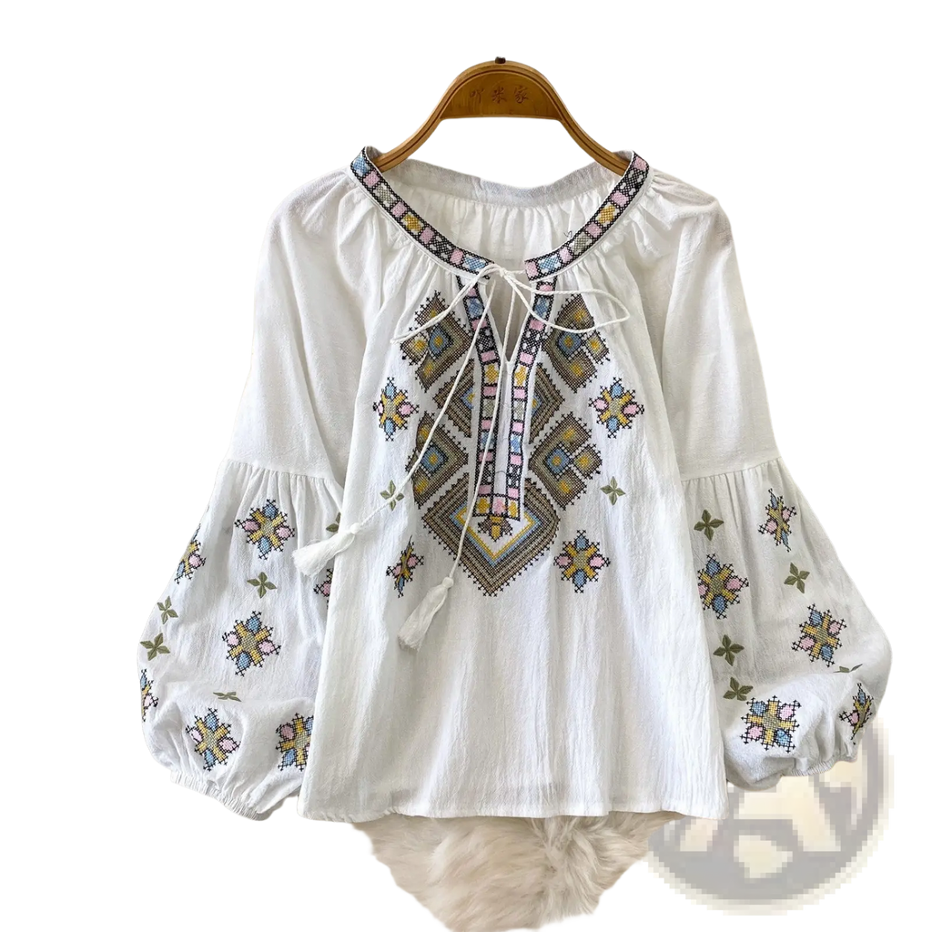 White embroidered lantern sleeve tie neck blouse with colorful geometric patterns and tassels on the neckline