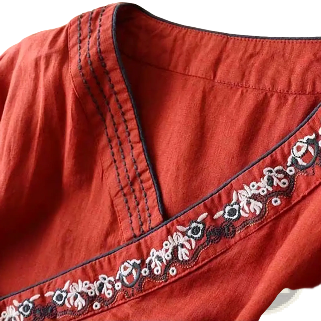A rust-colored embroidered linen wrap blouse with delicate white and black floral embroidery along the neckline