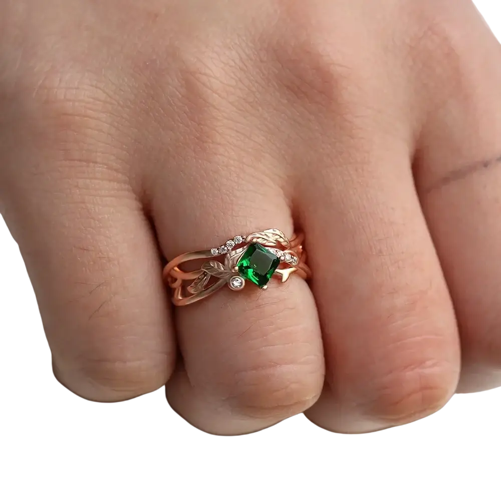 Rose gold ring with a square-cut emerald center stone and diamond leaf accents in an elegant design