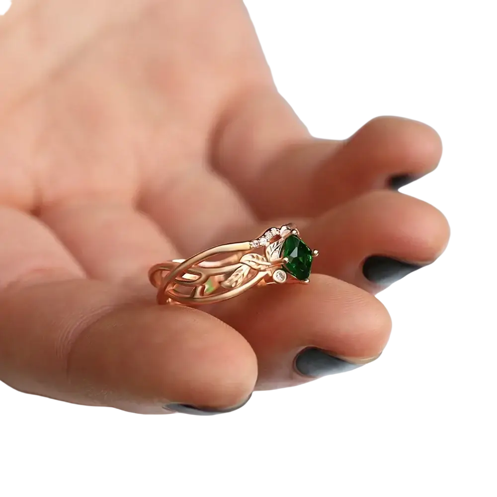 A delicate rose gold ring with a vibrant green emerald and diamond accents in an intricate leaf design