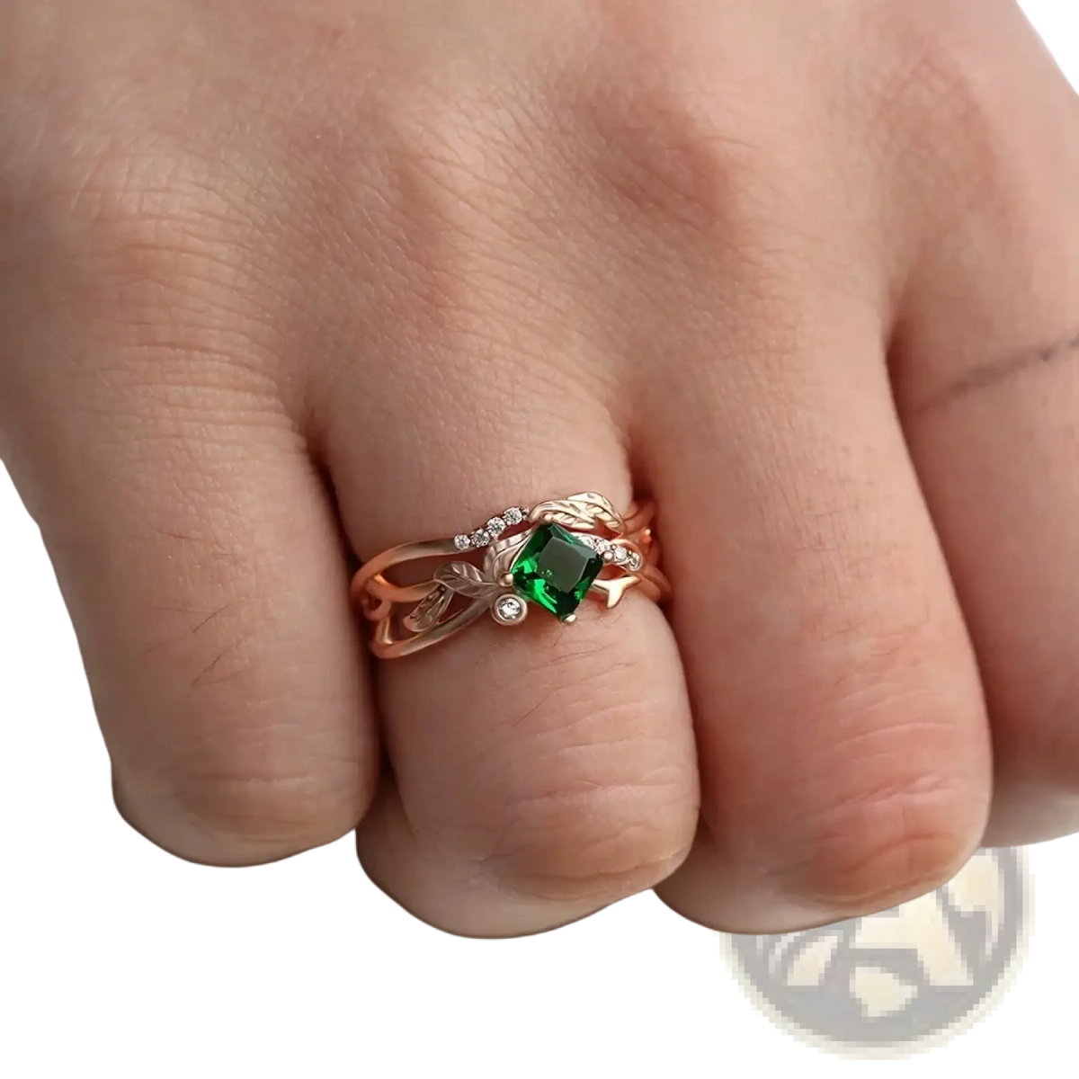 Rose gold ring with a square-cut emerald center stone and diamond leaf accents in an elegant design