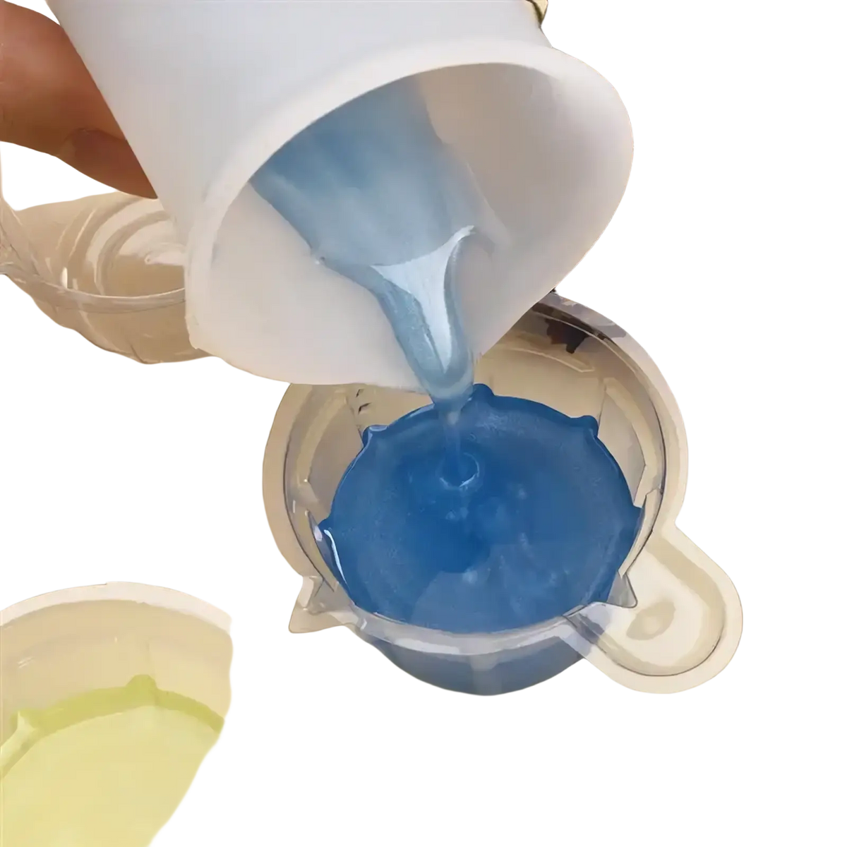 A translucent white plastic measuring cup pouring vibrant blue epoxy resin into a clear silicone mold for diy jewelry making
