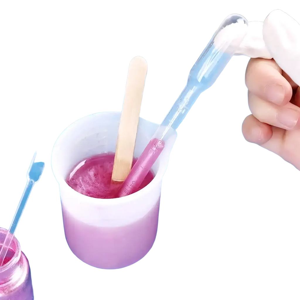 Transparent plastic pipette with white bulb transferring liquid into measuring cup with pink mixture for diy epoxy resin jewelry making