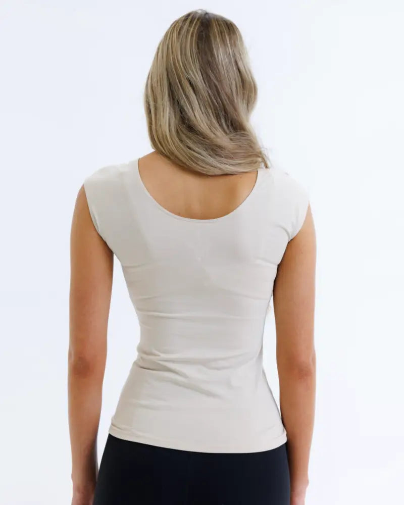 A woman wearing an essential tri-blend scoop neck fitted tee in cream with sleeveless design and rounded neckline