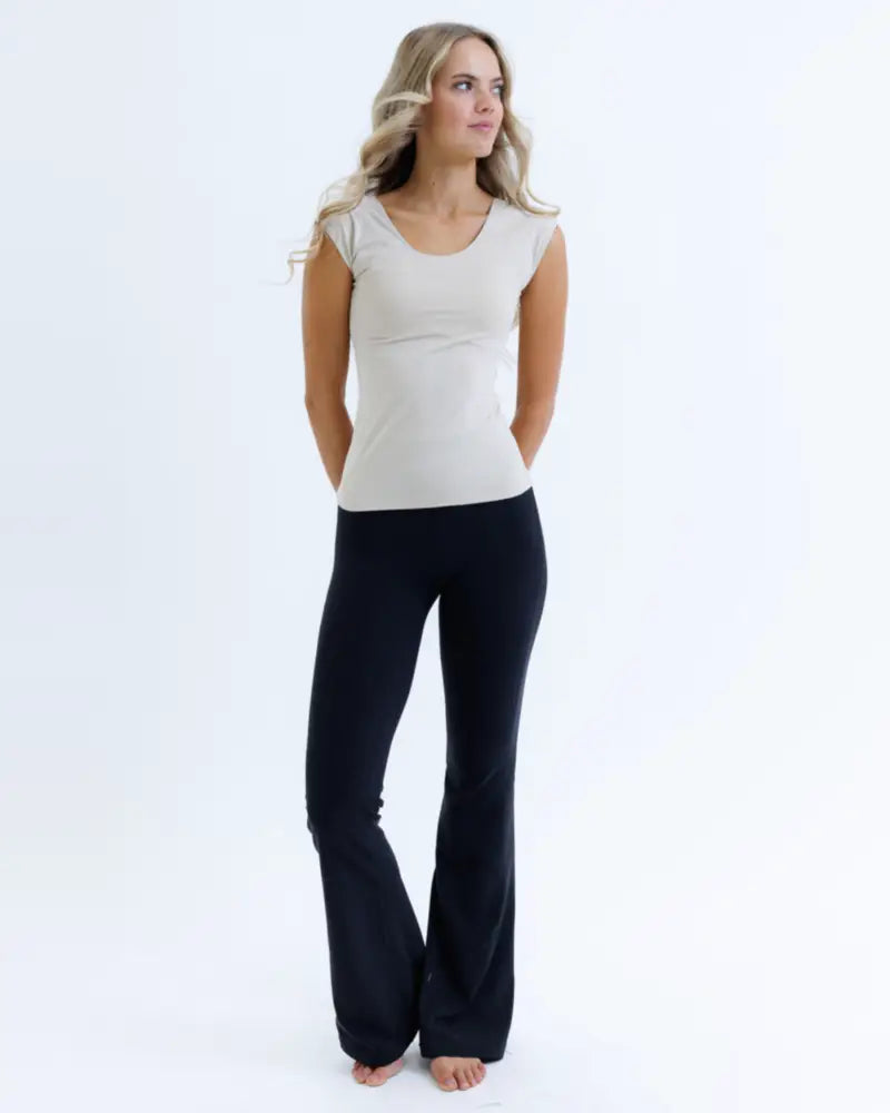 A woman wears a beige essential tri-blend scoop neck fitted tee paired with black flared pants