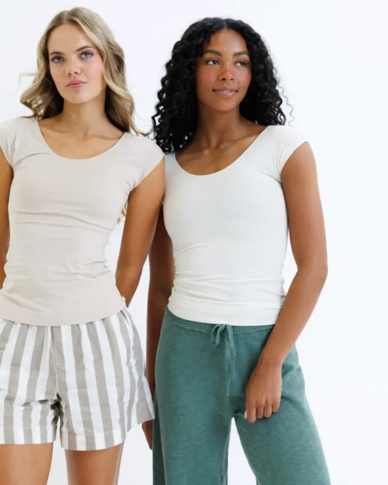 Two women model essential tri-blend scoop neck fitted tees in white paired with gray striped and solid teal pajama bottoms