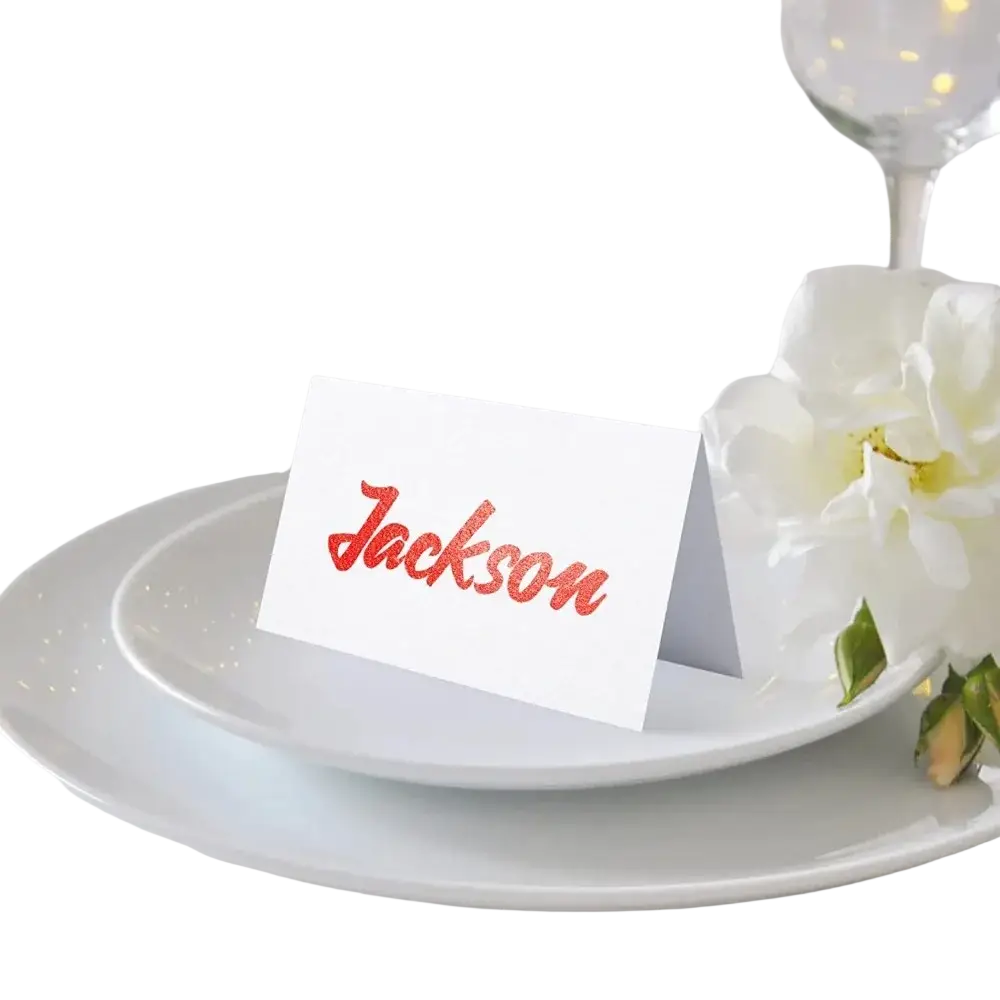 A white eucalyptus leaf place card with the name jackson in glittery red cursive script for wedding seating