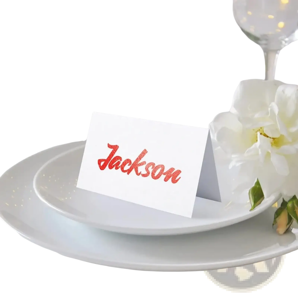A white eucalyptus leaf place card with the name jackson in glittery red cursive script for wedding seating